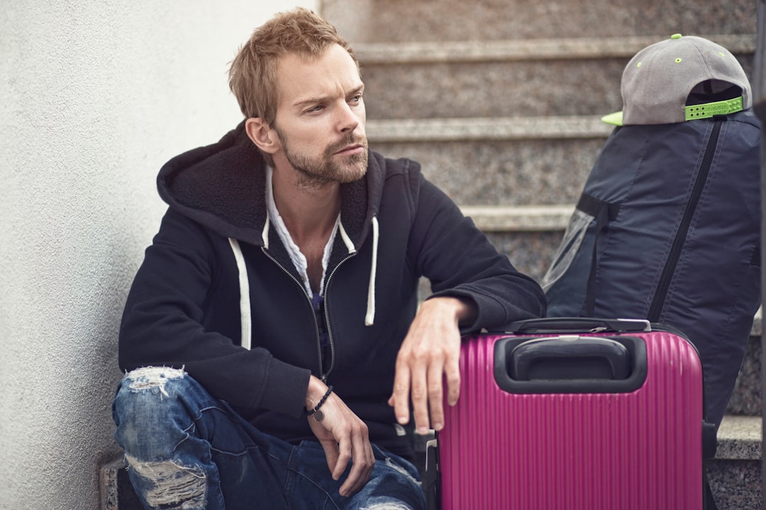 Photo by Sander Sammy a man sitting next to a purple suitcase