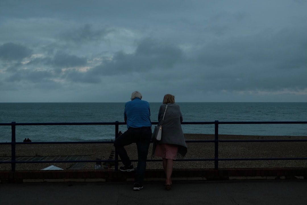 Photo by Al Elmes couple sitting on bench near sea during daytime