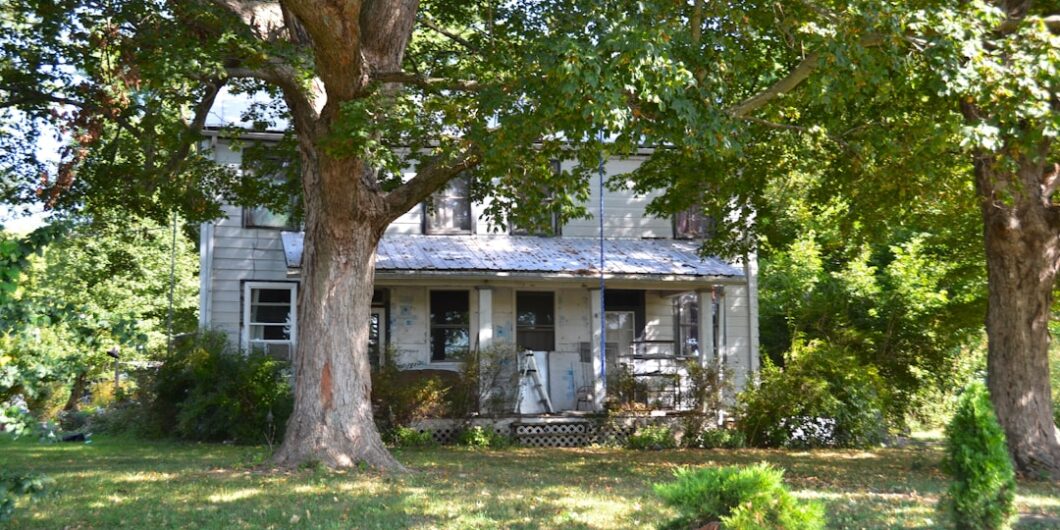 Old farmhouse surrounded by large trees and greenery.