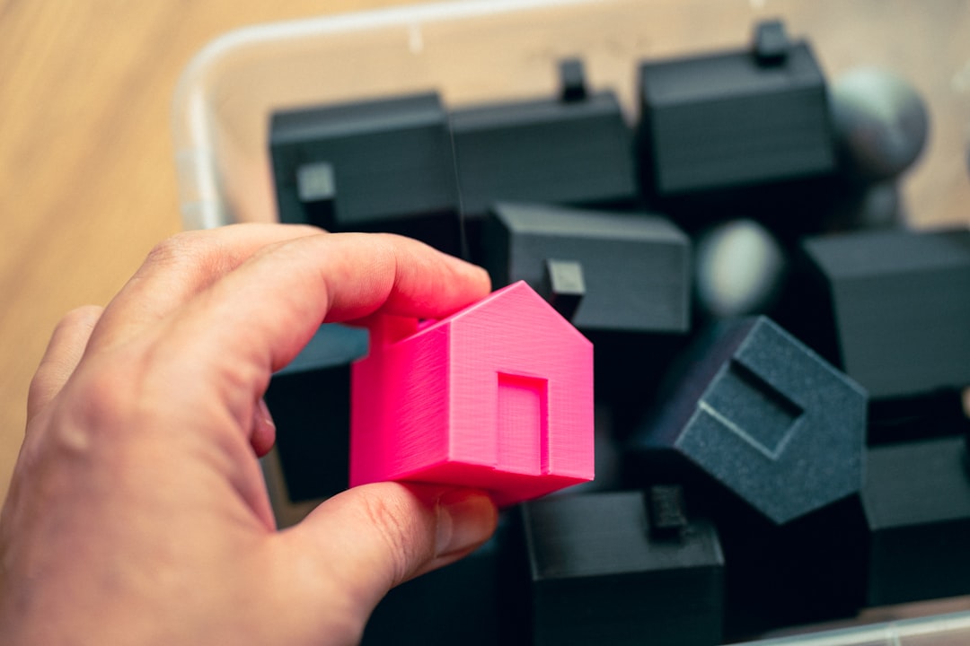 Photo by Jakub Żerdzicki A person holding a pink house in front of a pile of black cubes