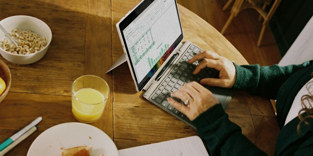 Person working on laptop at wooden table with breakfast.